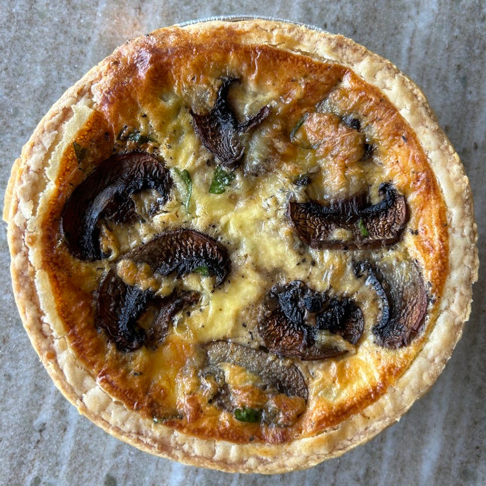 A top-down view of a baked mushroom and cheese quiche pie on a textured gray stone surface.